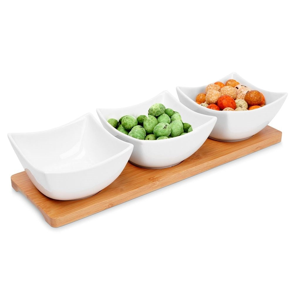 Three elegant porcelain bowls on a bamboo tray for snacks and dips
