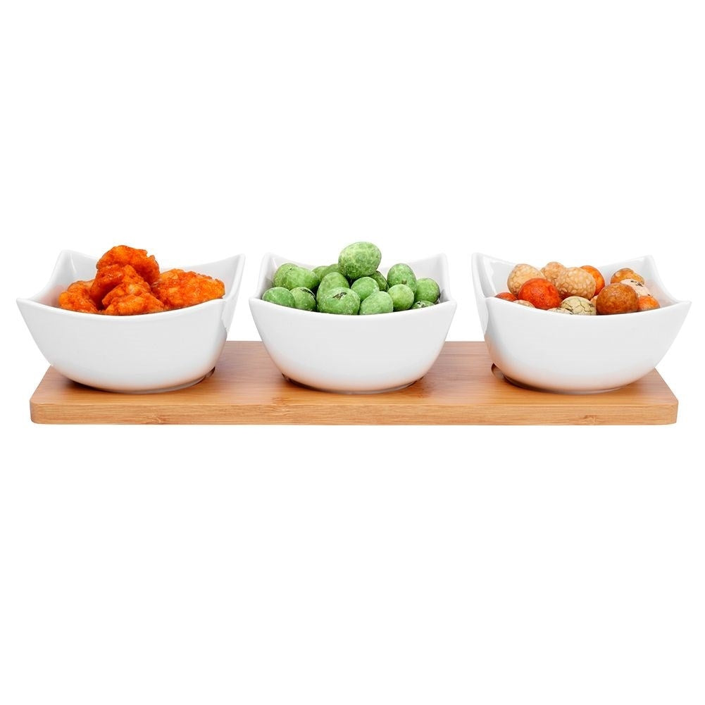 Three elegant porcelain bowls on a bamboo tray for snacks and dips