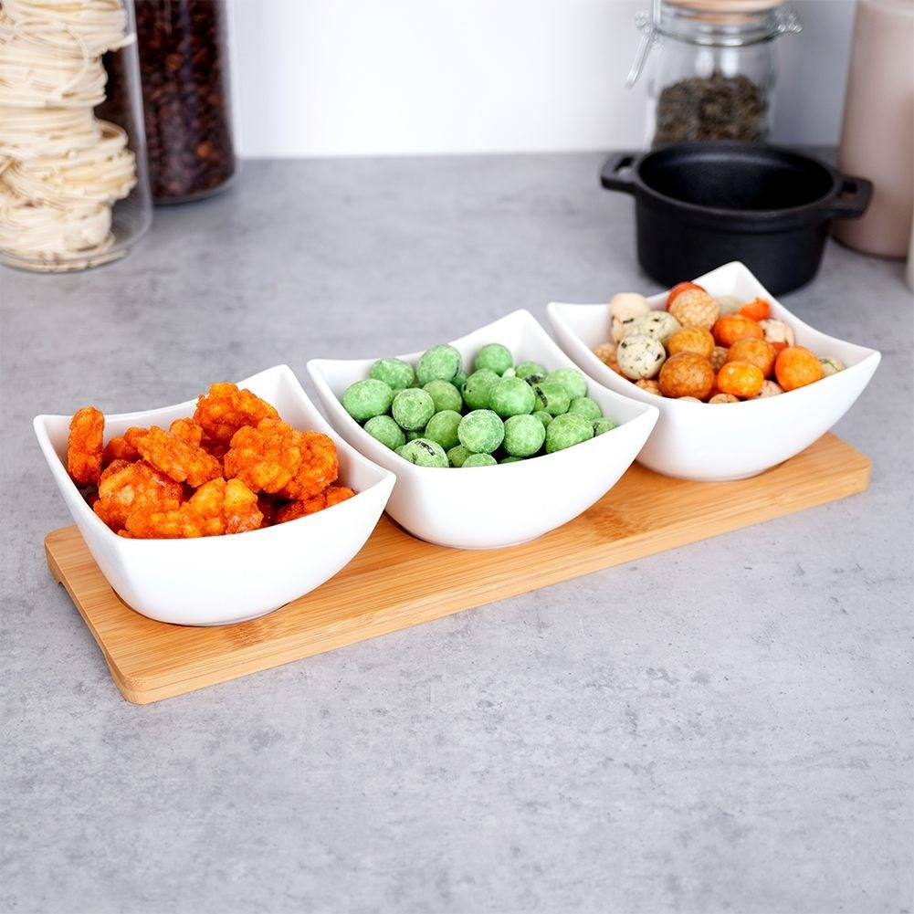 Three elegant porcelain bowls on a bamboo tray for snacks and dips