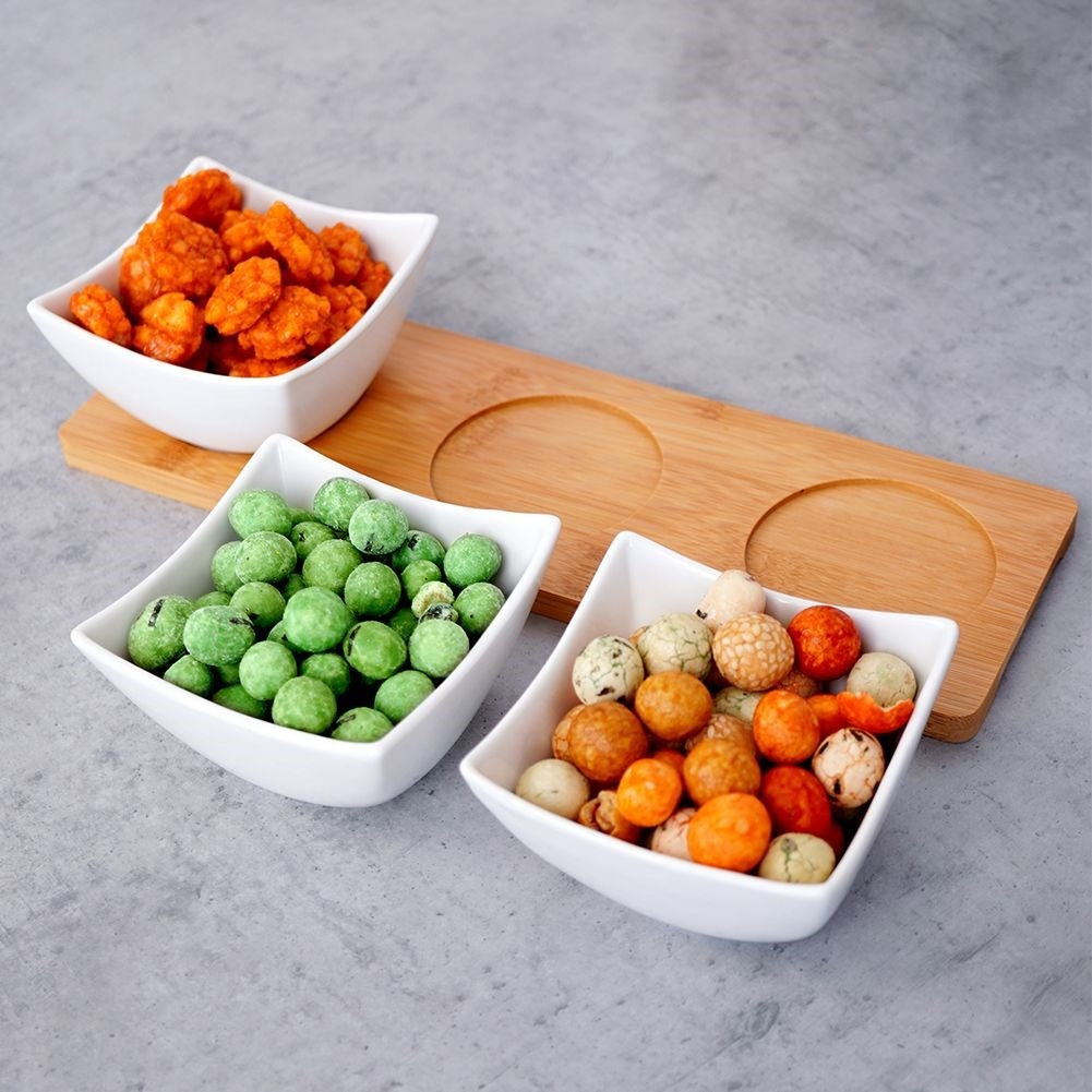 Three elegant porcelain bowls on a bamboo tray for snacks and dips