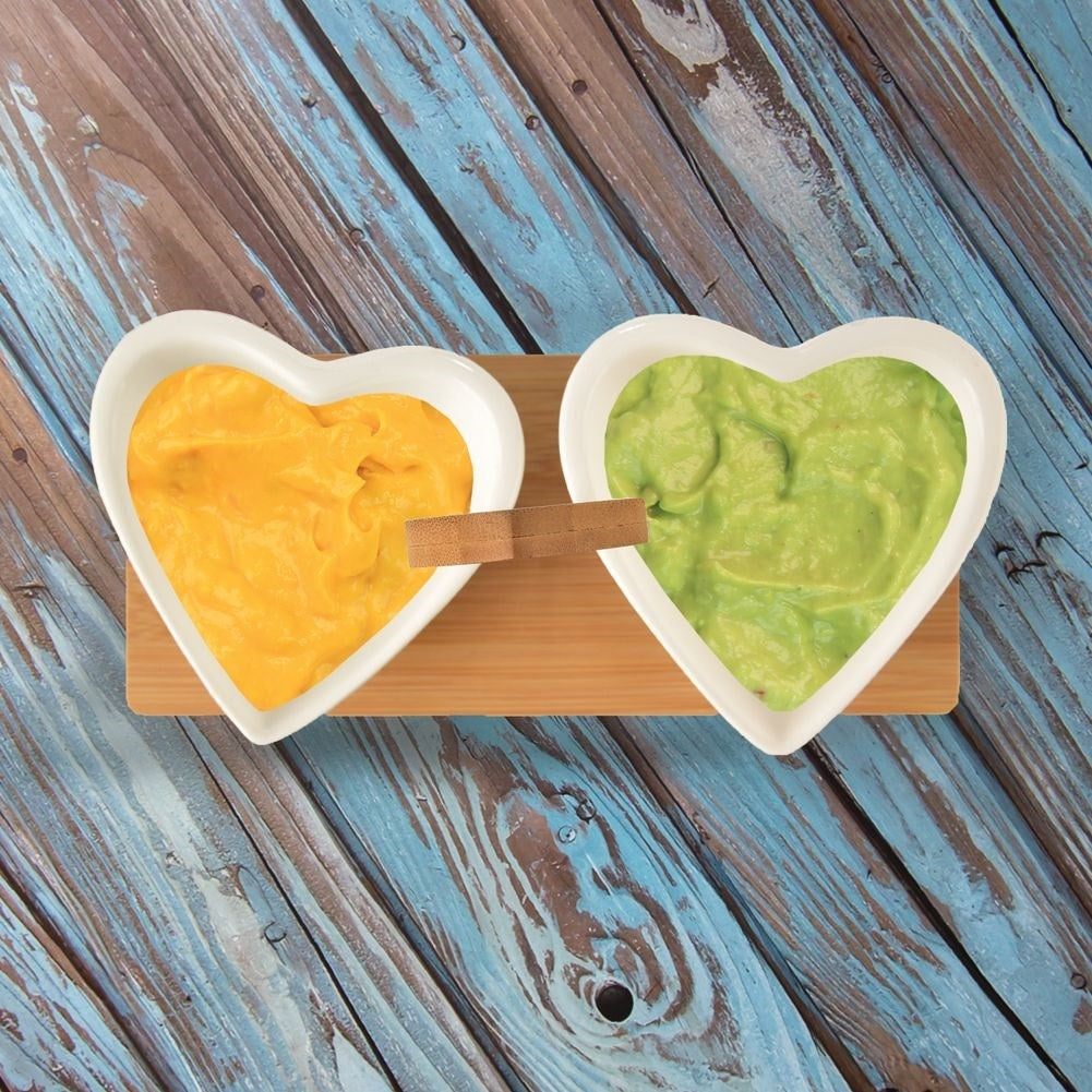 Two heart-shaped porcelain bowls on a bamboo tray for serving